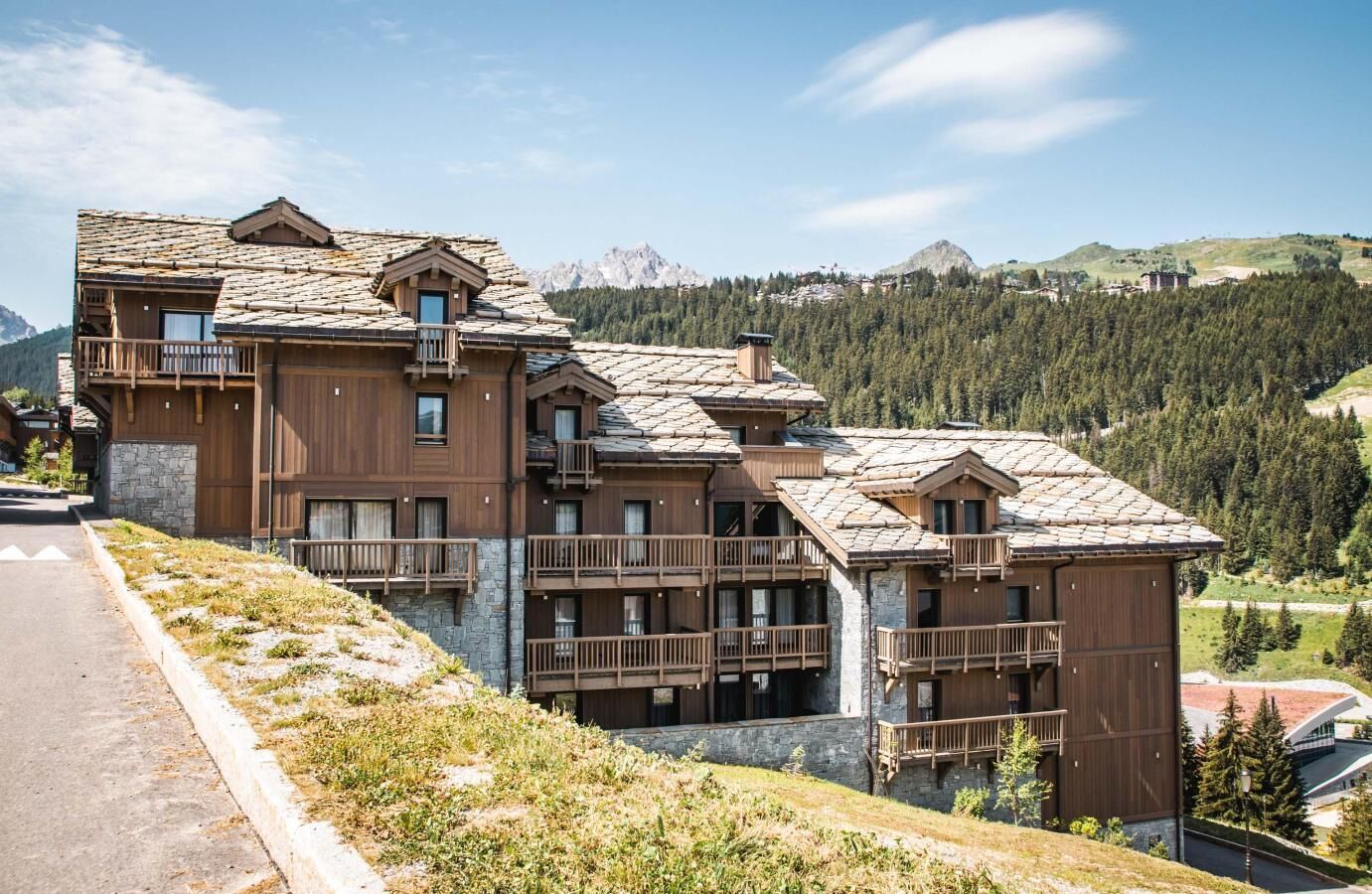 A multi-story hotel with wooden balconies and a mountainous backdrop.