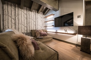 A modern living room with a sofa, a mounted TV, and decorative wall shelves. - Wifi, 200m from resort center, 5th floor, view exceptional/mountain, sauna, terrace, balcony (Courchevel)