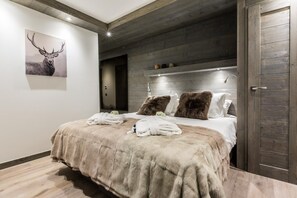 A modern bedroom with a large bed, a wooden headboard, a mounted deer painting, and a rustic wooden door.