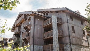 A multi-story wooden building with balconies and stone pillars. - Wifi, 150m from ski slopes, 2nd floor, view mountain, sauna, balcony, fireplace or stove, parking (Courchevel)