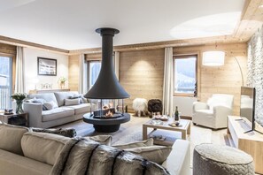 A cozy living room with a central fireplace, wooden walls, and a sofa with fur throw. - Wifi, 150m from ski slopes, 2nd floor, view mountain, sauna, balcony, fireplace or stove, parking (Courchevel)