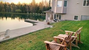 Ett hus med en stor veranda med utsikt över en lugn sjö, omgivet av träd.