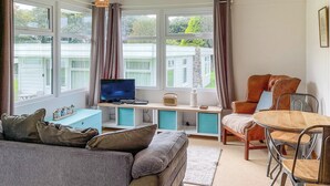 A cozy living room with a sofa, a wooden table, and a TV on a built-in shelf. - 2 bedroom accommodation in Roch, near Haverfordwest (Roch, near Haverfordwest)