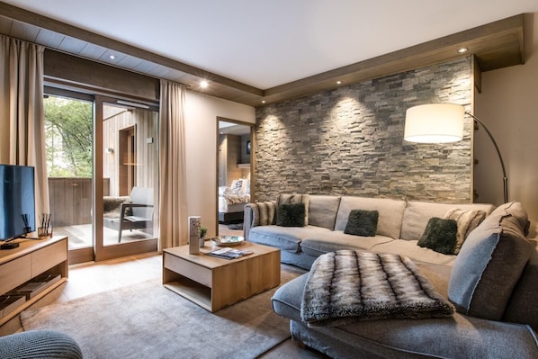 A modern living room with a stone accent wall, a large sofa, a coffee table, and a TV on a wooden stand.