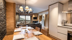 Un coin repas avec une table en bois dressée pour six personnes, un lustre et une vue sur les montagnes grâce à de grandes fenêtres.