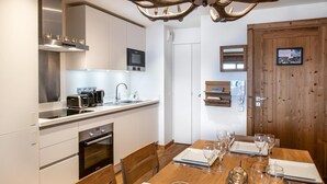 Une cuisine moderne dotée d’appareils électroménagers en acier inoxydable, une table à manger dressée pour six personnes avec des verres à vin, et une porte en bois ornée d’un cadre de photo.