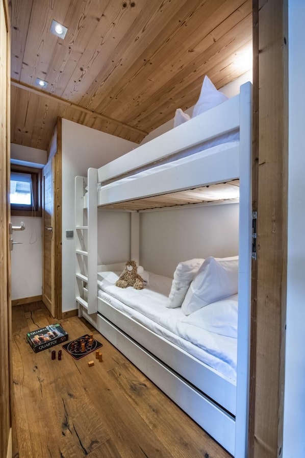 A bunk bed room with wooden ceiling and white bedding.