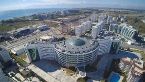 Un grand hôtel circulaire, doté d’un dôme central, entouré de bâtiments modernes et offrant une vue sur la côte.