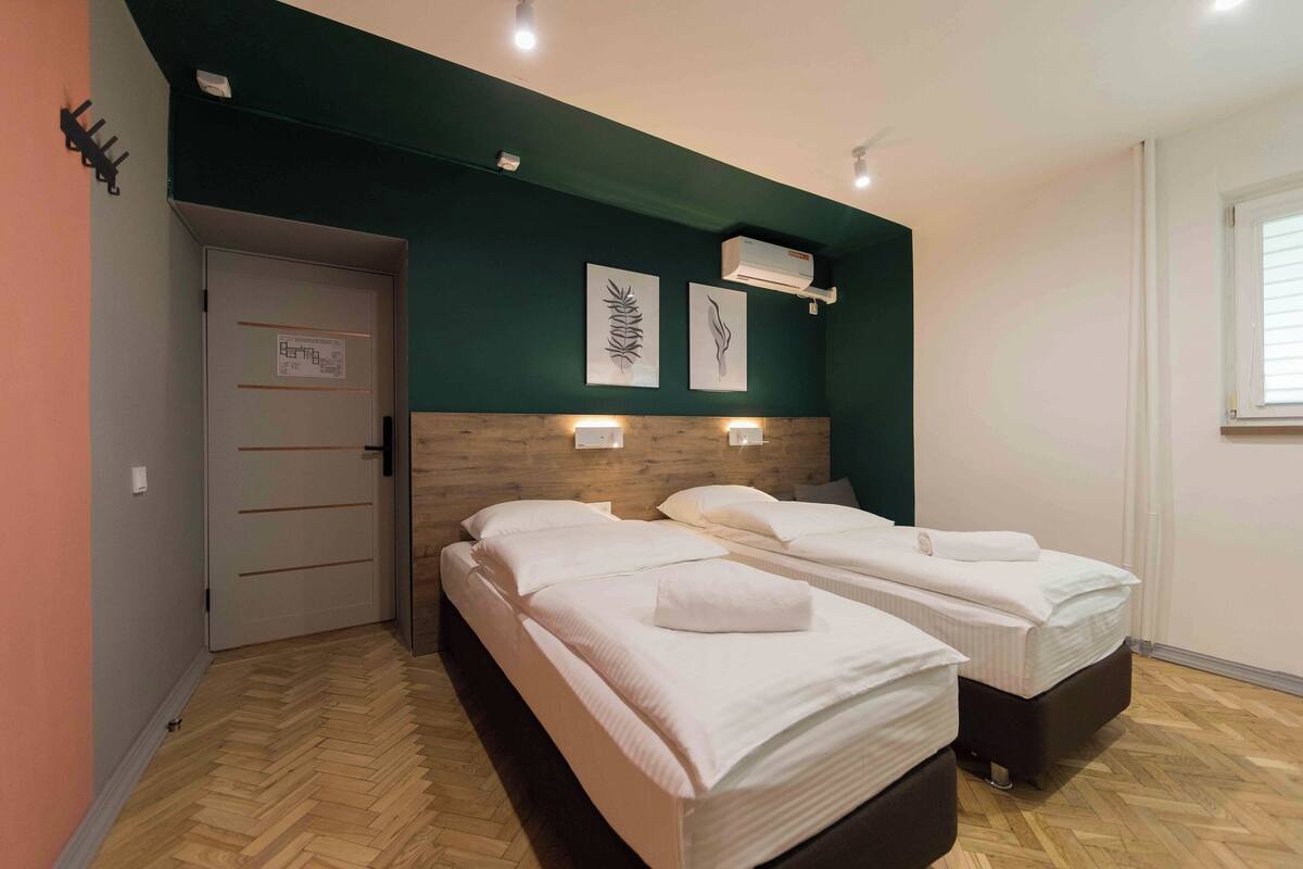 A hotel room with two beds, a wooden floor, and artwork on the wall.