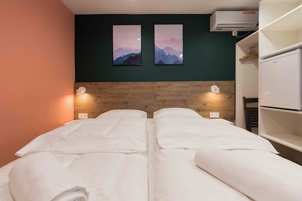 A double bed with white linens, two wall-mounted night lights, and two framed paintings of mountains. - Urban Rooms (Minsk)