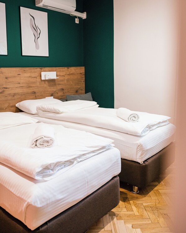 A hotel room with two beds, a wooden headboard, a green wall, and a wooden floor. - Urban Rooms (Minsk)