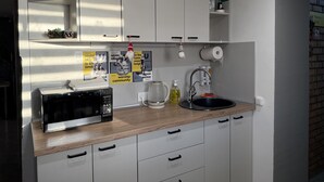 A modern kitchen with white cabinets, a microwave, a sink, and a clock on the wall. - Urban Rooms (Minsk)