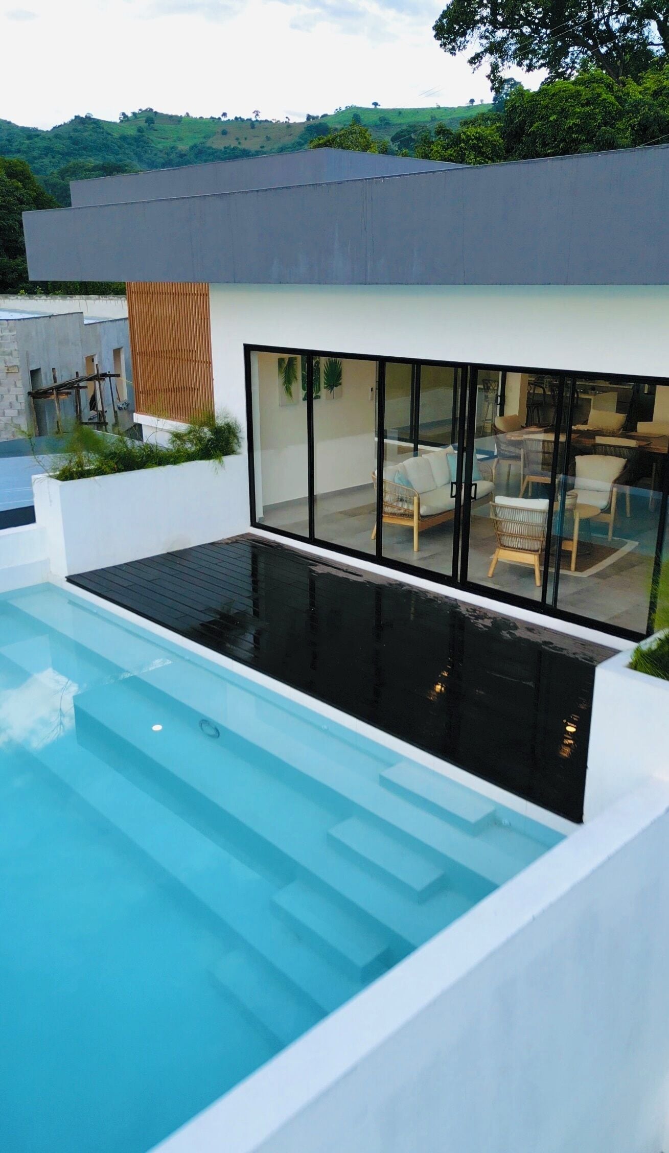 Une maison moderne dotée d’une piscine, de grandes fenêtres et offrant une vue sur les collines.