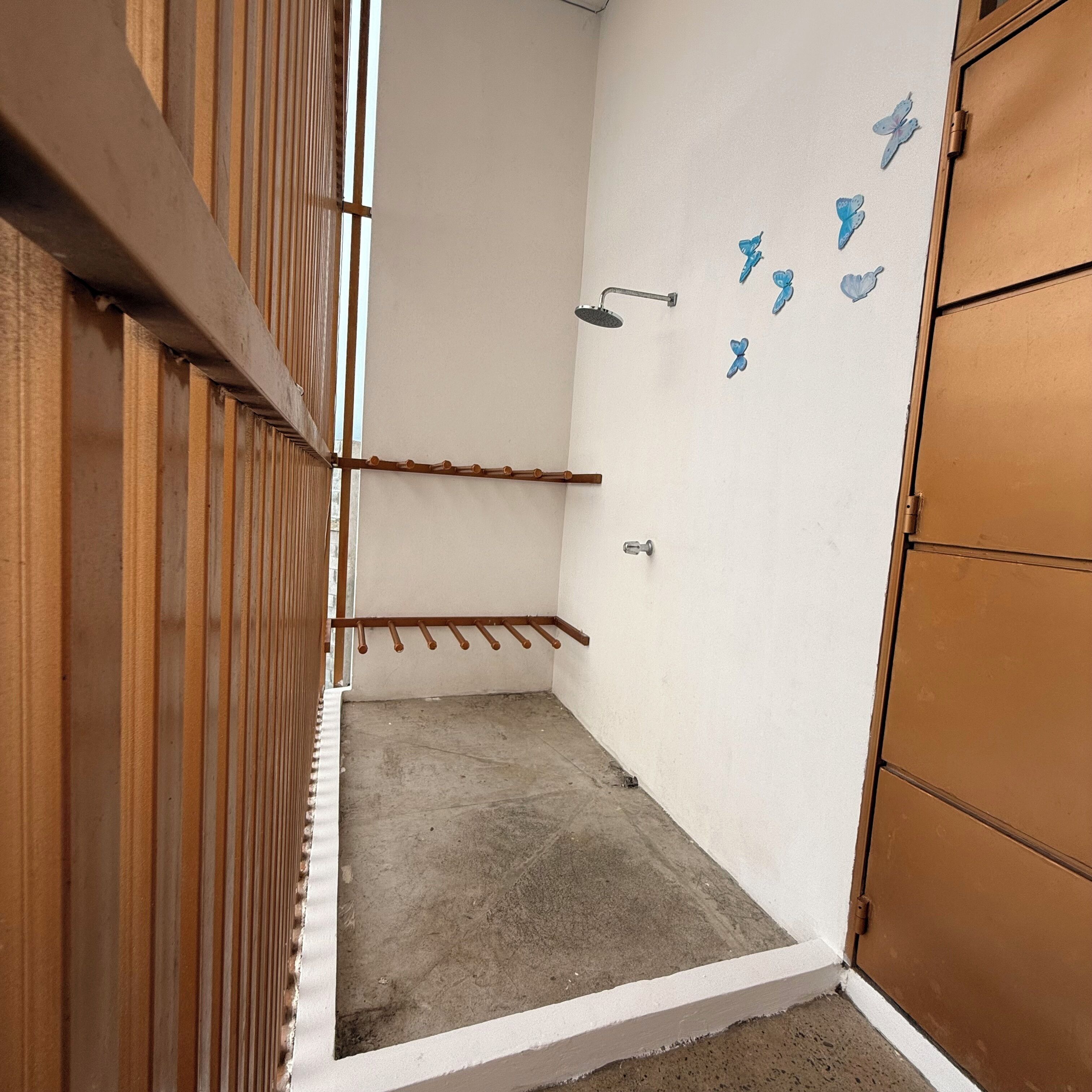 A small, enclosed room with a concrete floor, a wooden door, and a white wall with a shower area.