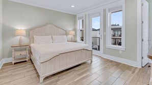 Un dormitorio con una cama grande, dos mesitas de noche con lámparas, un ventilador de techo y vistas al balcón exterior.