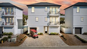 Un moderno edificio residencial con garaje, un carro de golf rojo y un camino de entrada bien cuidado.