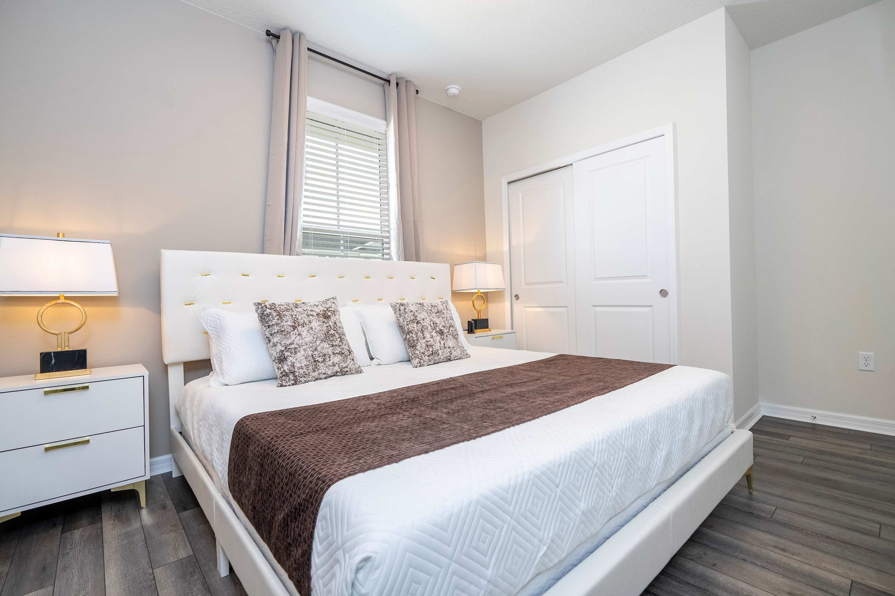 A bedroom with a large bed, two bedside tables with lamps, a wardrobe, and a window with curtains.