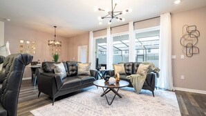 A spacious living room with a black leather sofa, a round coffee table, and a chandelier. - Family Friendly 5Bd Close to Disney Windsor Cay 1269 (Clermont)