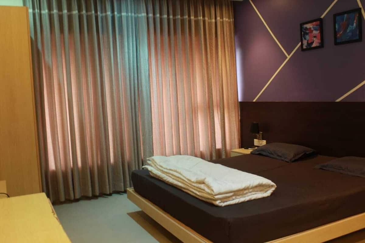 A hotel room with a bed, curtains, a nightstand, and two framed pictures on the wall.