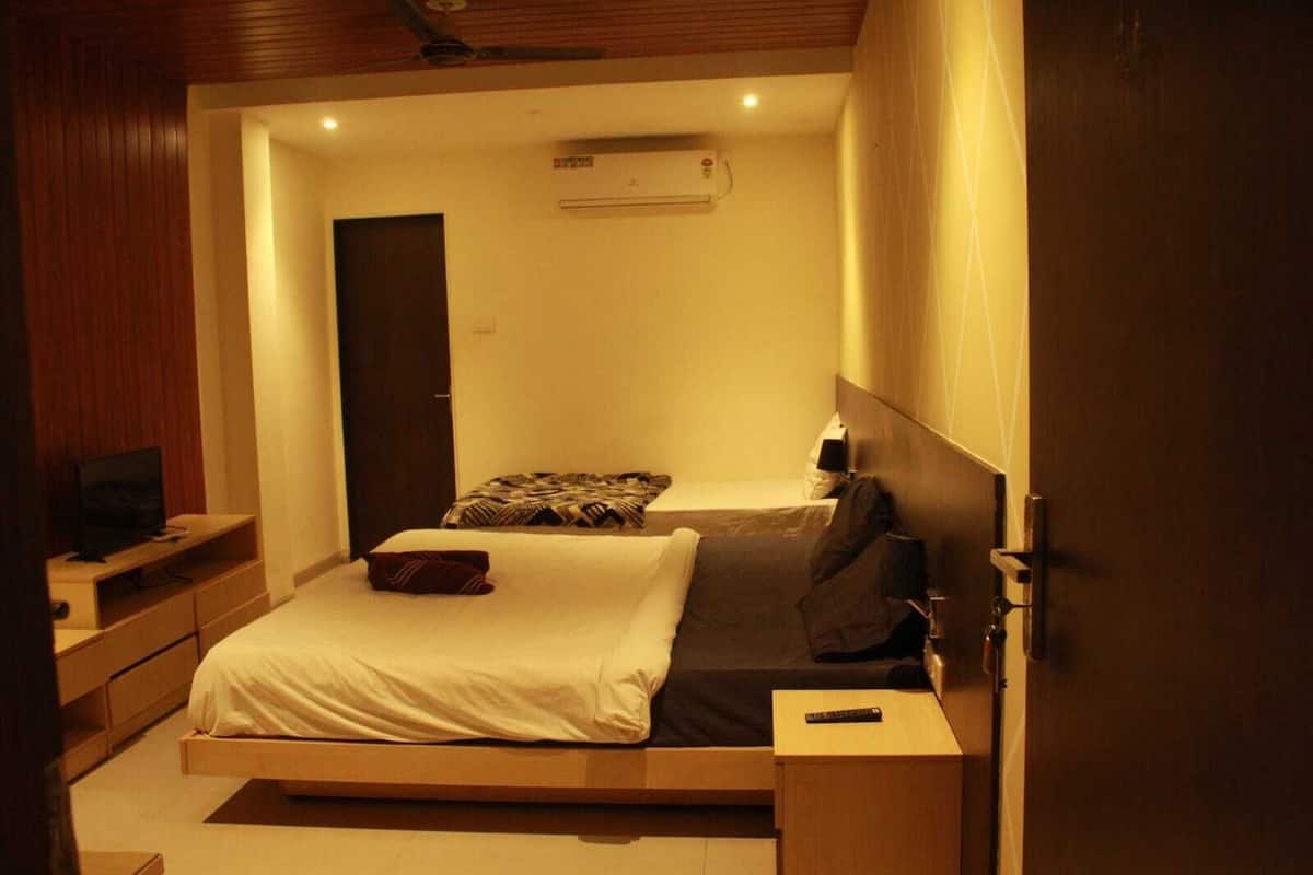 A bedroom with a bed, a TV, a bedside table, and an air conditioning unit.
