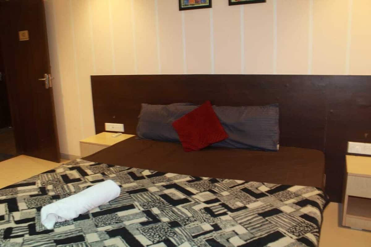 A hotel room with a bed, a nightstand, a wall-mounted TV, and a door.
