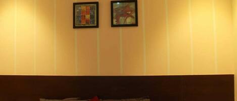 A hotel room with a bed, two framed pictures on the wall, and a power outlet on the side.