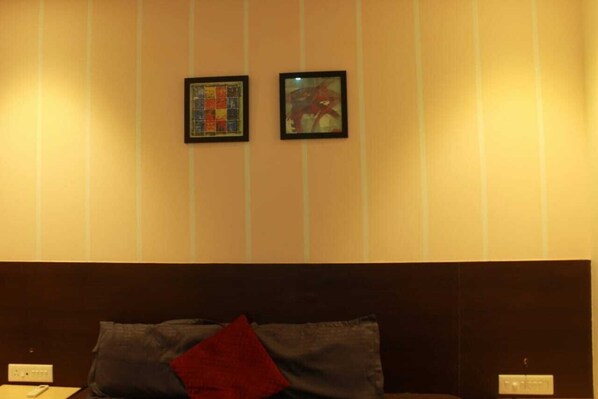 Habitación de hotel con cama, dos cuadros en la pared y un enchufe lateral.