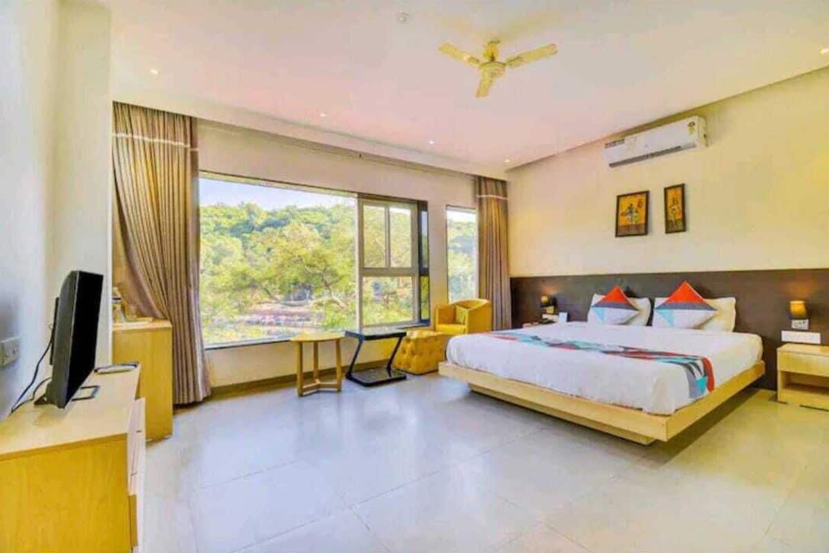 A modern hotel room with a large bed, a desk, a chair, and a TV.