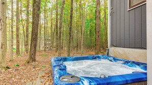 A hot tub in a forested area with a wooden deck and a building in the background.