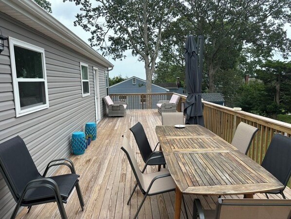A wooden deck with a table and chairs, a covered seating area, and a view of a house.