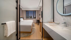Ein modernes Hotelzimmer mit einem großen Bett, einem Schreibtisch, einem Badezimmer mit Spiegel und Blick auf die Stadt.
