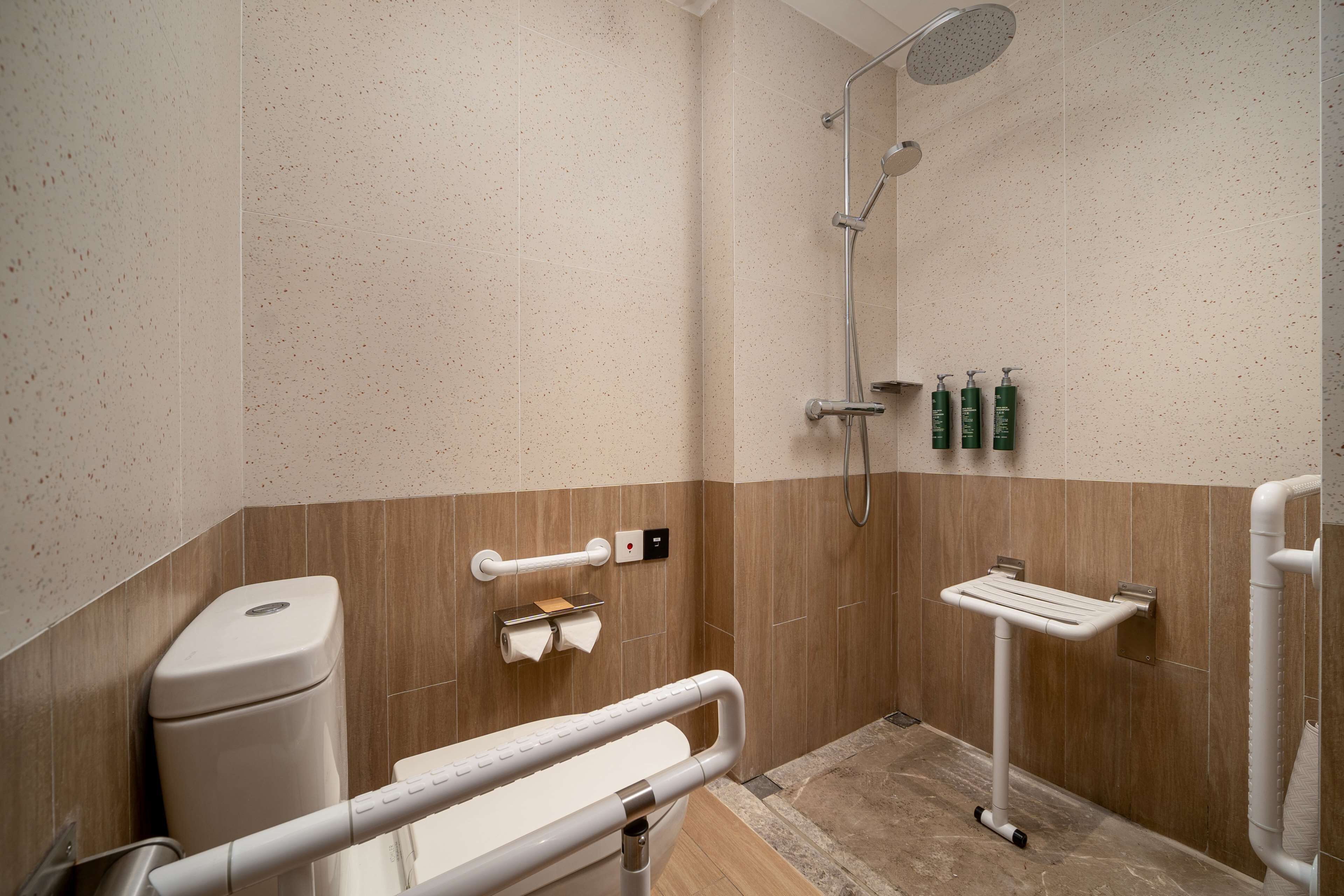 Un baño moderno con ducha, inodoro, barras de apoyo y un perchero para toallas.