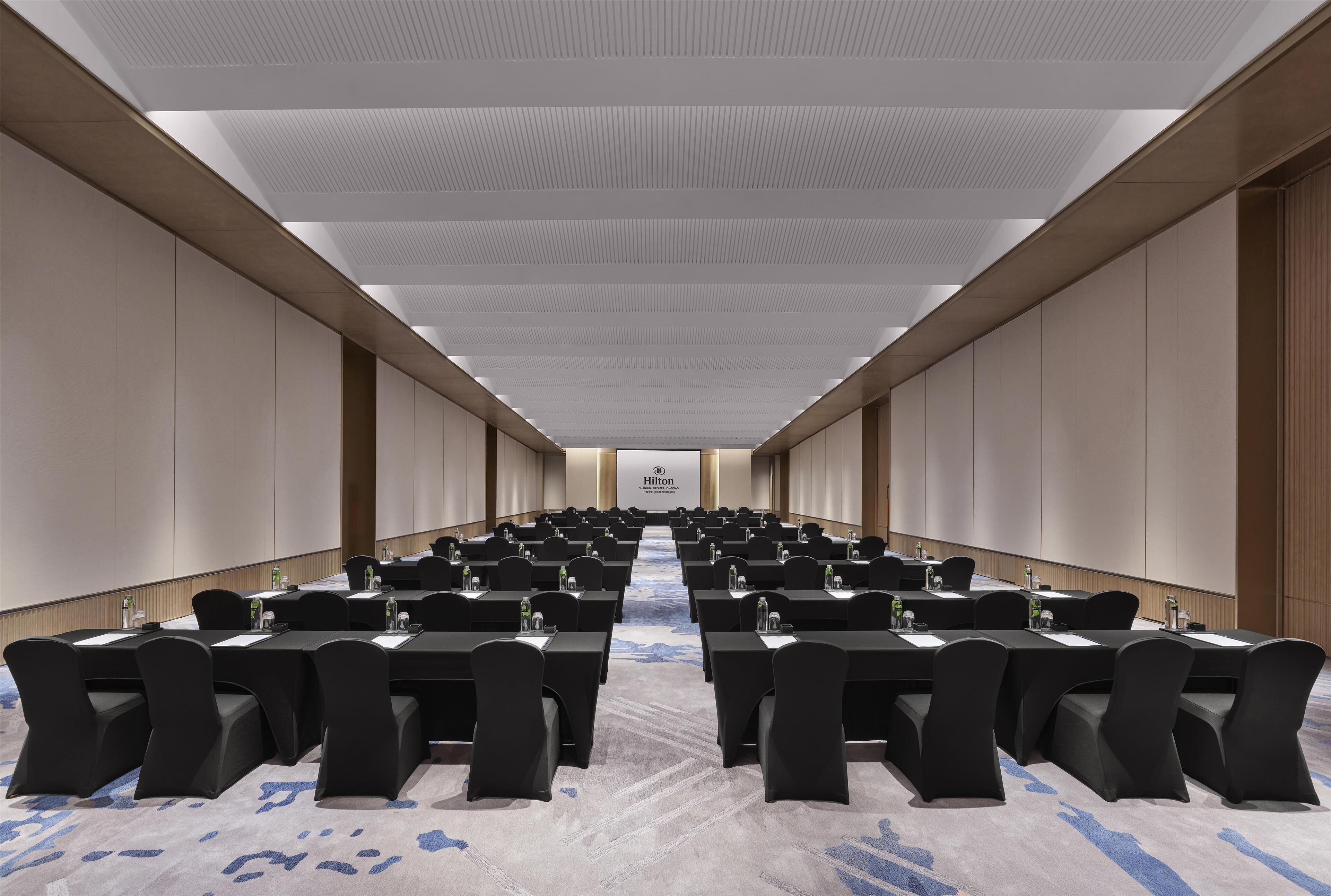 A conference room with long tables and chairs, a carpeted floor, and a ceiling with recessed lighting.