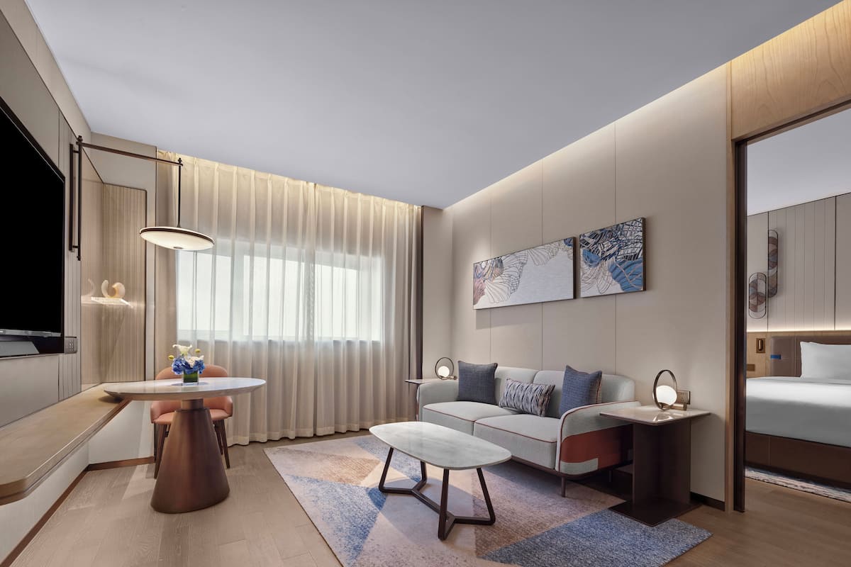 Une chambre d’hôtel moderne, équipée d’un canapé, d’une petite table, d’un téléviseur et ornée d’œuvres d’art au mur.
