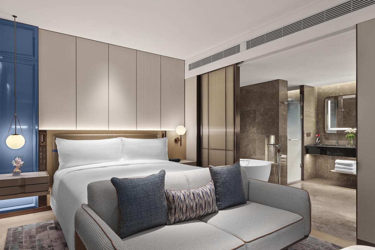 Une chambre d’hôtel moderne avec un grand lit, un canapé, une salle de bain avec un miroir et une douche.