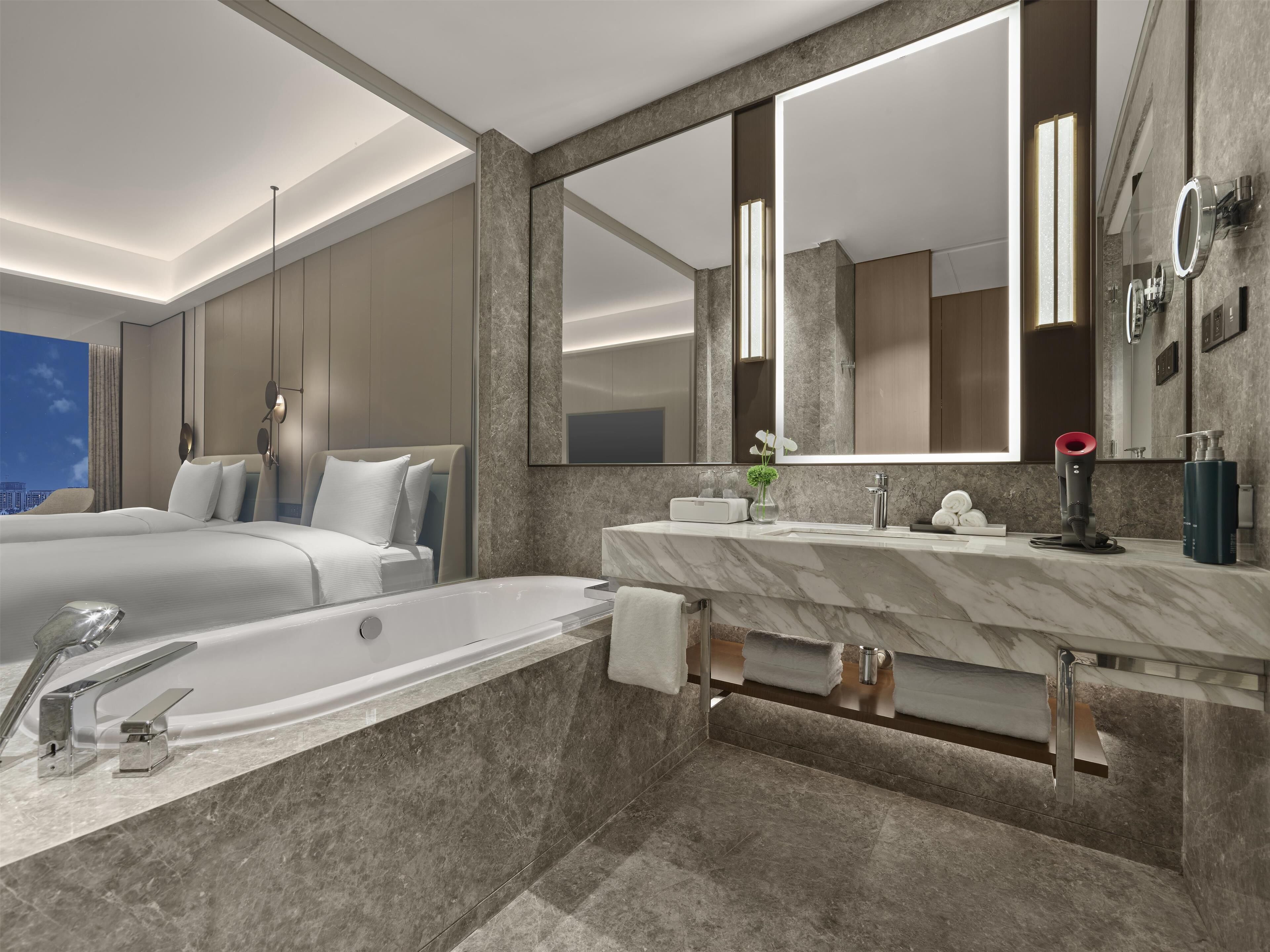 A modern bathroom with a large mirror, a bathtub, and a vanity with a marble countertop.