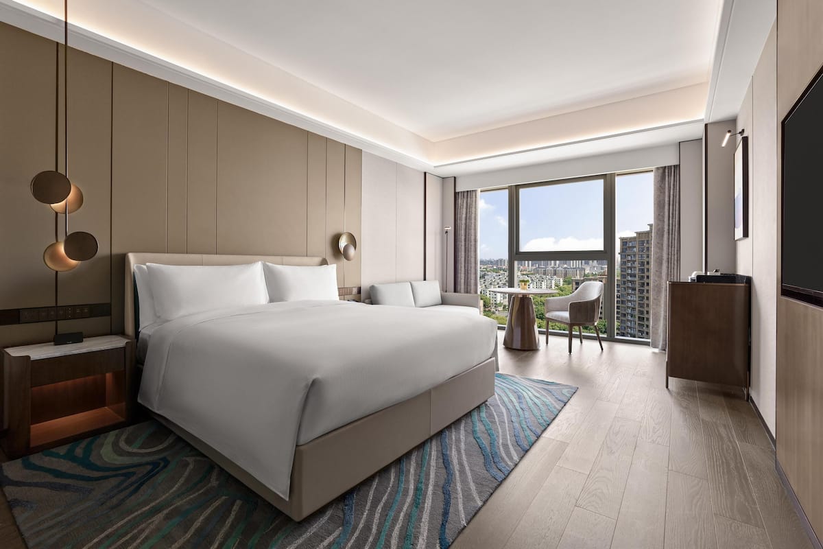 Une chambre d’hôtel moderne dotée d’un grand lit, d’un bureau, d’une chaise et offrant une vue sur la ville grâce à de grandes fenêtres.