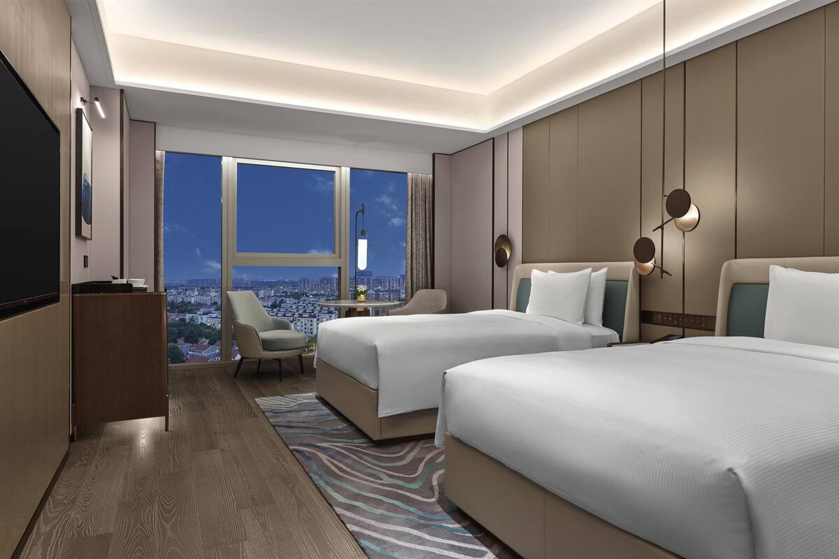 Une chambre d’hôtel moderne avec deux lits, un coin salon, une télévision et une vue sur la ville.