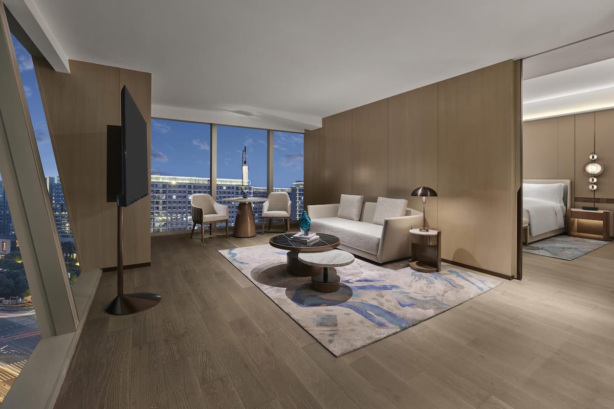 Une chambre d’hôtel moderne avec une grande fenêtre, un canapé, une table basse et un téléviseur.