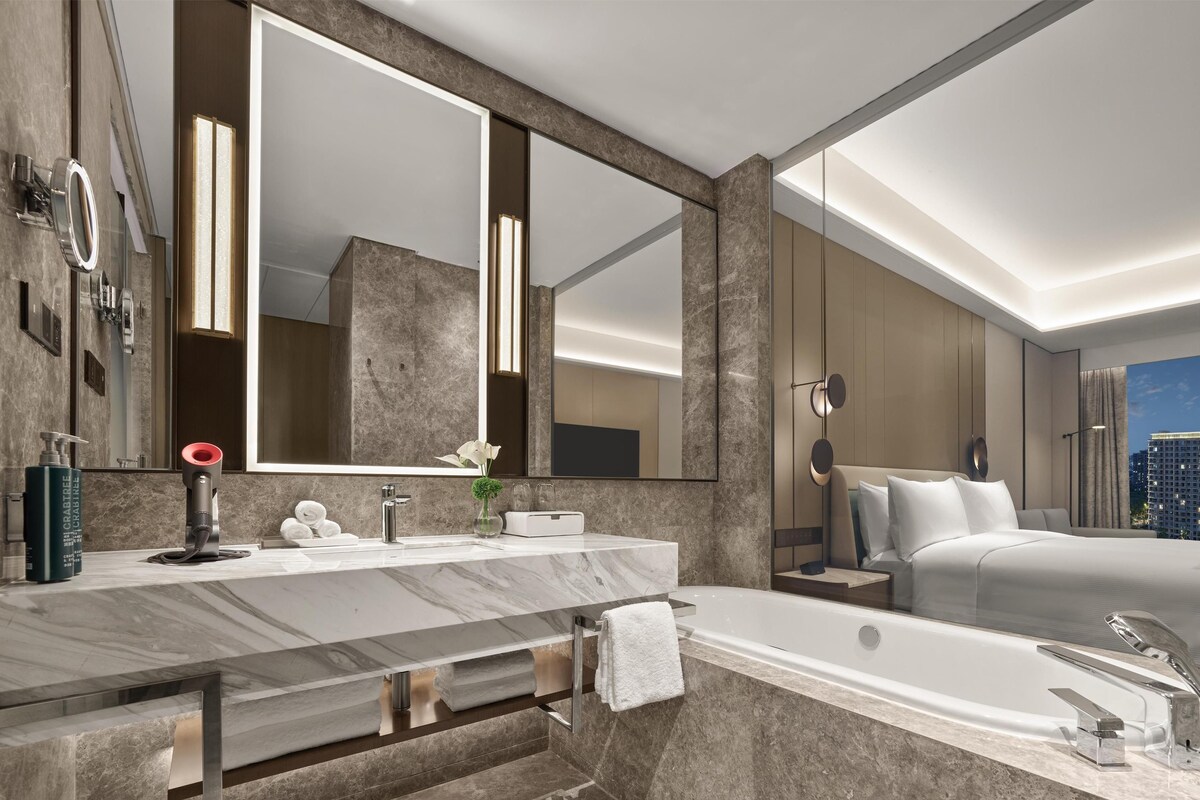 Une salle de bain moderne dotée d’un grand miroir, d’une baignoire et d’un meuble-lavabo avec un plan de travail en marbre.