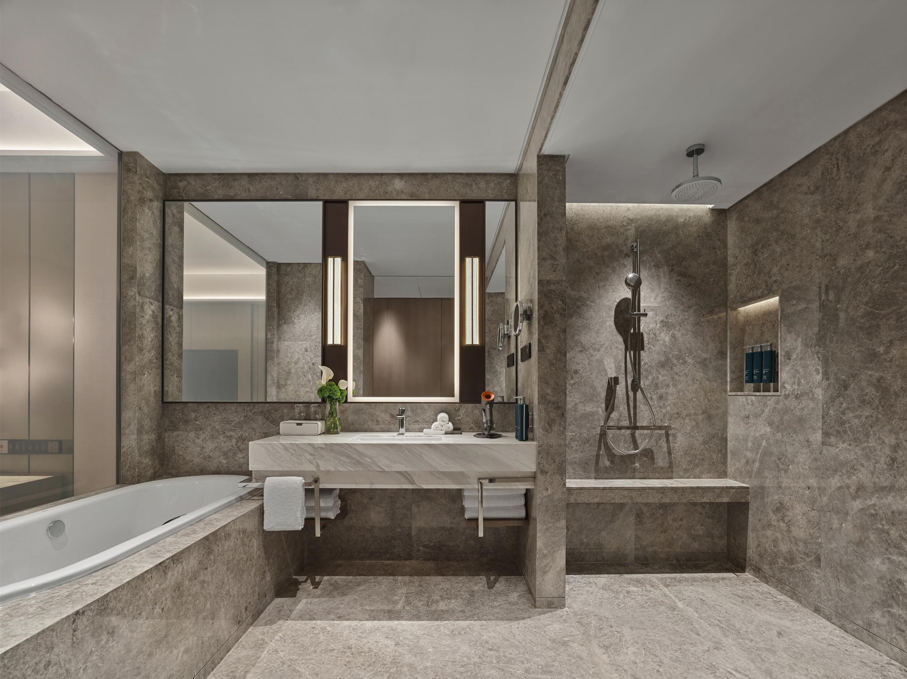 Un baño moderno con un espejo grande, una bañera, una ducha y paredes de mármol.