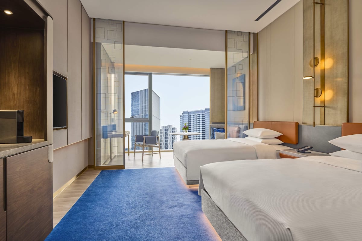 Ein Hotelzimmer mit zwei Betten, einem Schreibtisch, einem Fernseher und Blick auf die Stadt.