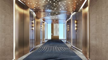 A modern hallway with a patterned carpet, recessed lighting, and a view into a room with a large window.
