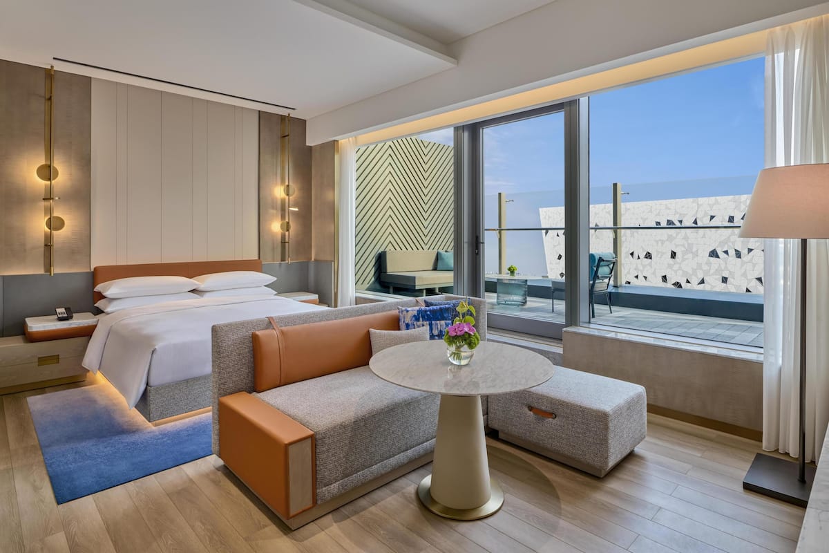 Ein modernes Hotelzimmer mit Bett, Sofa, rundem Tisch und einem Balkon mit Blick.