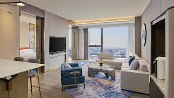Ein modernes Hotelzimmer mit großem Fenster, Flachbildfernseher, Sofa, Couchtisch und Essbereich.