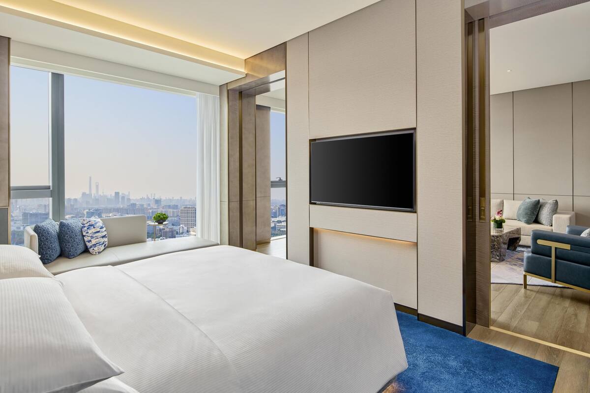 Ein modernes Hotelzimmer mit einem großen Bett, einem Fernseher, einer Couch und Blick auf die Stadt.