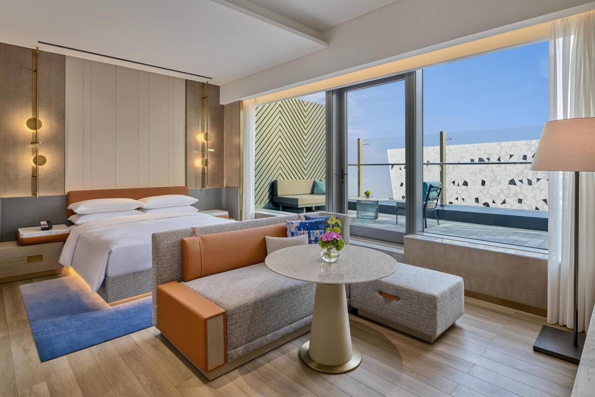 Ein modernes Hotelzimmer mit Bett, Sofa, rundem Tisch und einem Balkon mit Blick.