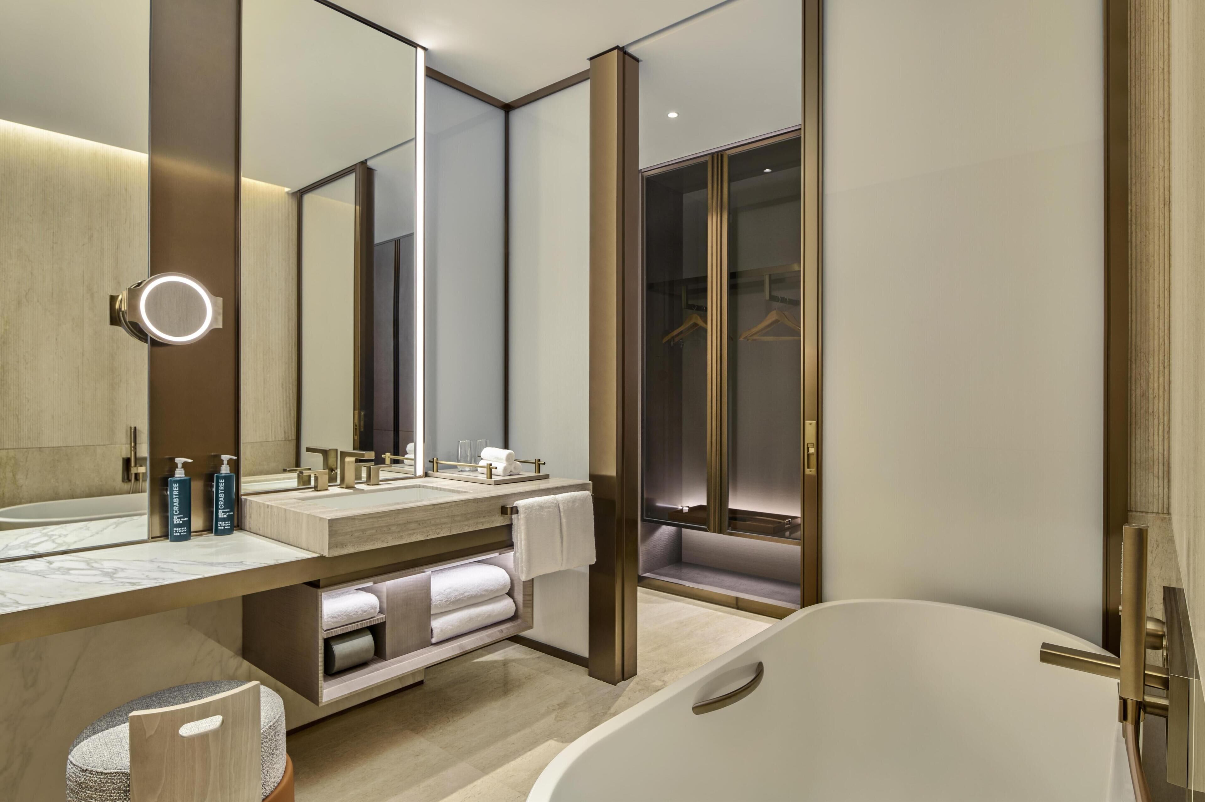 Ein modernes Badezimmer mit großem Spiegel, einer Badewanne und einem begehbaren Kleiderschrank.