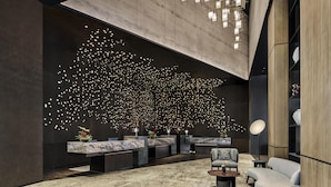 Een moderne lobby met een marmeren receptiebalie, een zithoek en een opvallende verlichtingsinstallatie aan het plafond.