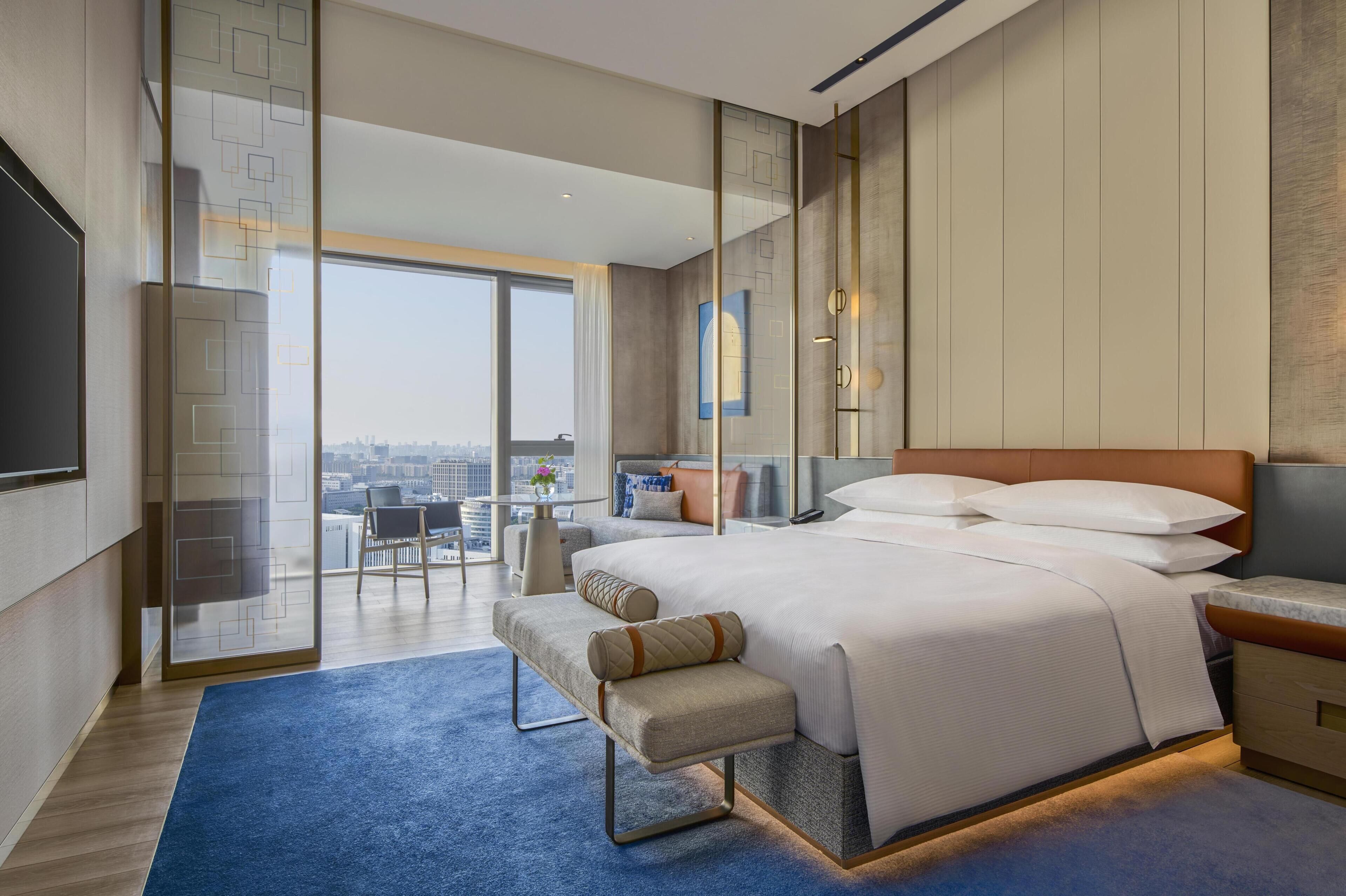 Une chambre d’hôtel moderne dotée d’un grand lit, d’un bureau, d’une chaise, d’une télévision et offrant une vue sur la ville.